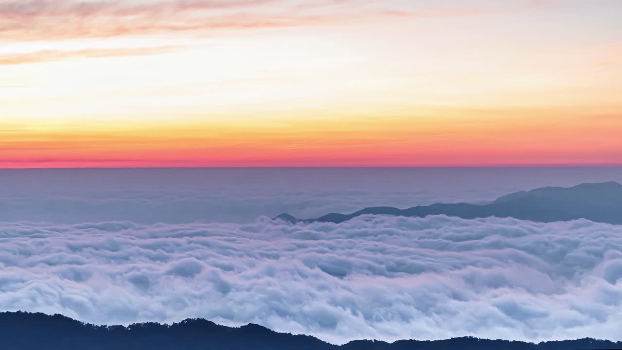 Experience the awe-inspiring beauty of nature as mountain peaks pierce through a vast sea of clouds during a tranquil sunrise. The sky transitions from deep blue to warm hues of orange and pink