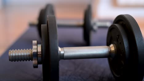 a rack focus shot between two dumbbells lying on a yoga mat. a cinematic close-up of free weights for a home workout or strength training session