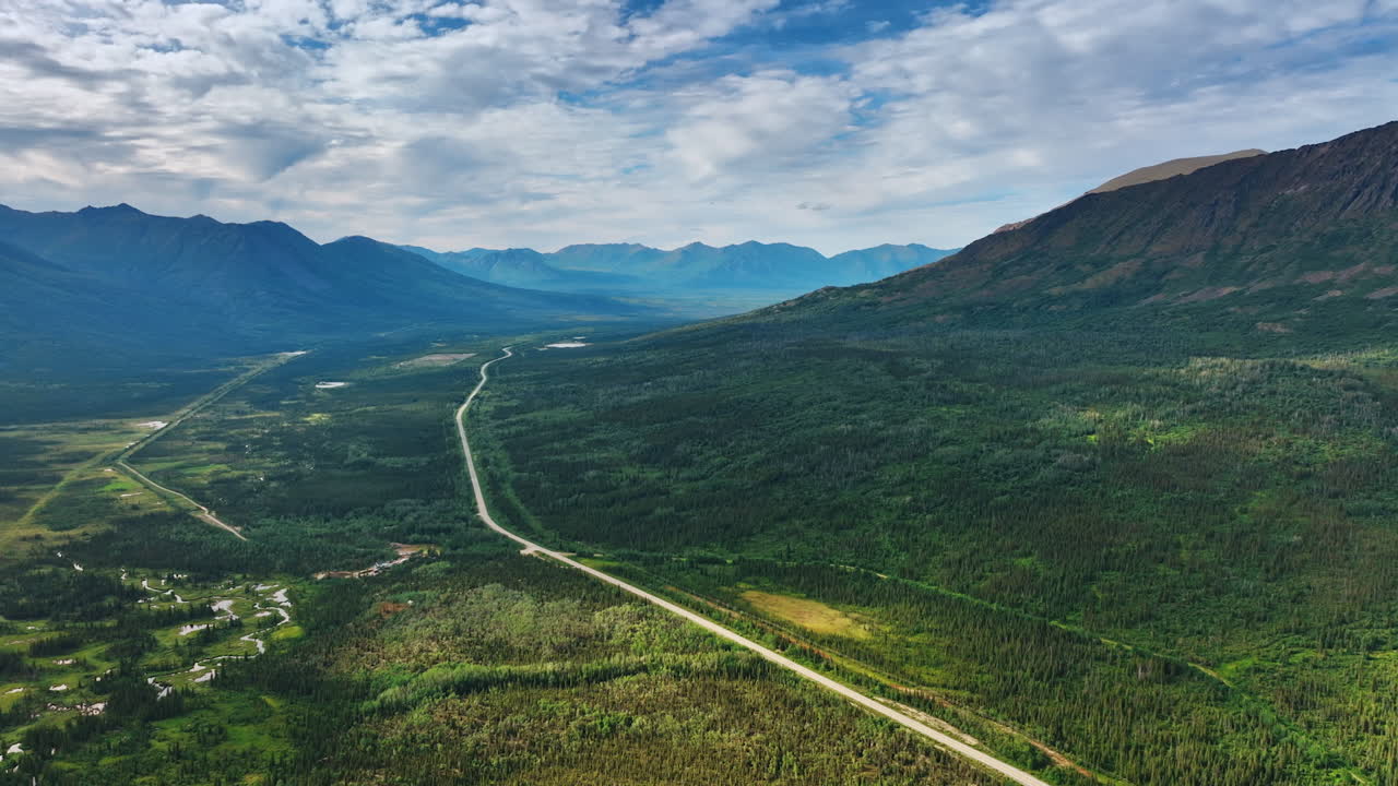 Highway and Forest Valley Leading to Distant Mountain Range. An expansive perspective shows a straight highway running through a wide green valley and boreal forest