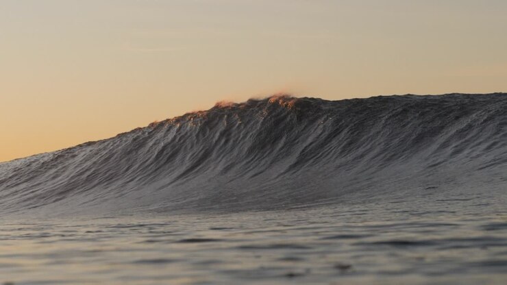 A short heavy wave crash over the shallow rock ledge as the sun rises in the background