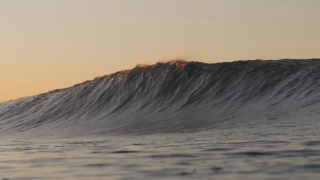 a short heavy wave crash over the shallow rock ledge as the sun rises in the background