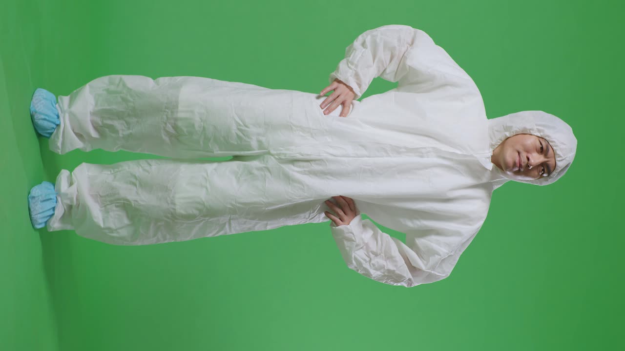 cuerpo lleno de científico masculino asiático poniendo las manos en la cadera y mirando a su alrededor en el fondo de la pantalla verde