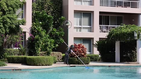 worker methodically cleans a large outdoor pool