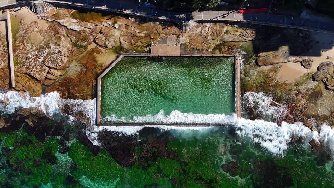 Aerial rock pool surrounded by ocean waves in Cronulla near rocky headland, Sydney NSW Australia