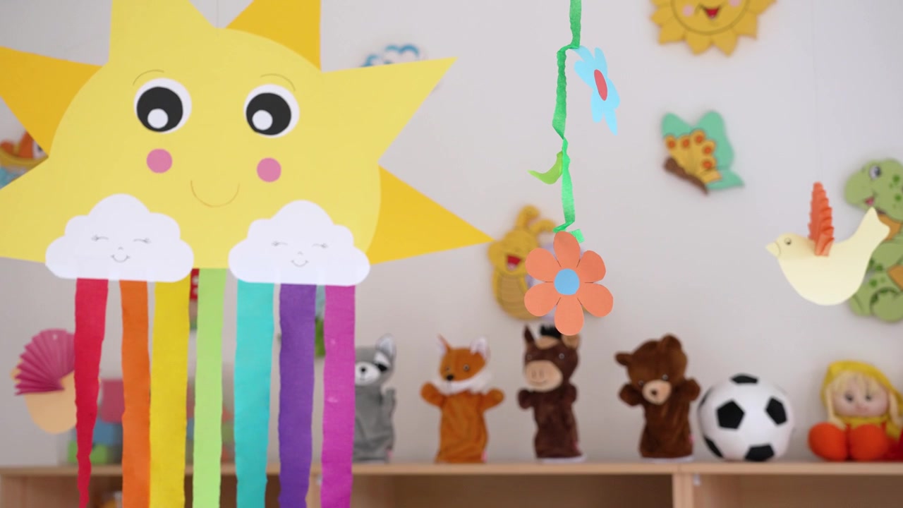 Verspielte Papierdekorationen und Handpuppen schaukeln sanft in einem hell dekorierten Spielzimmer.