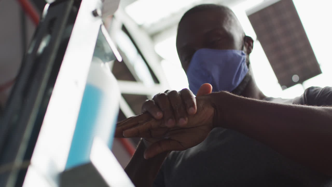Fit african american man wearing face mask sanitizing his hands in the gym