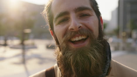 Primer-Plano-Retrato-De-Un-Joven-Feliz-Y-Barbudo-Hipster-Sonriendo-Alegre-Disfrutando-Del-Estilo-De-Vida-Urbano-De-La-Ciudad-Viajando