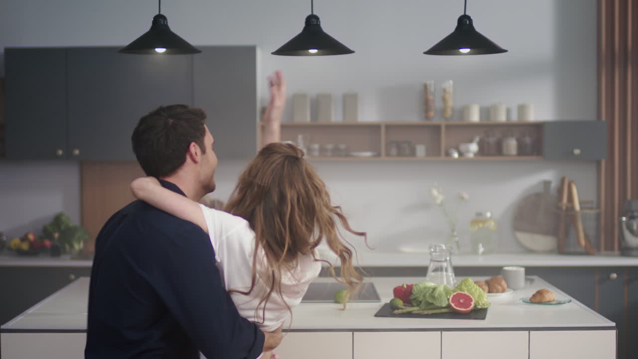 una pareja joven bailando juntos en la cocina.