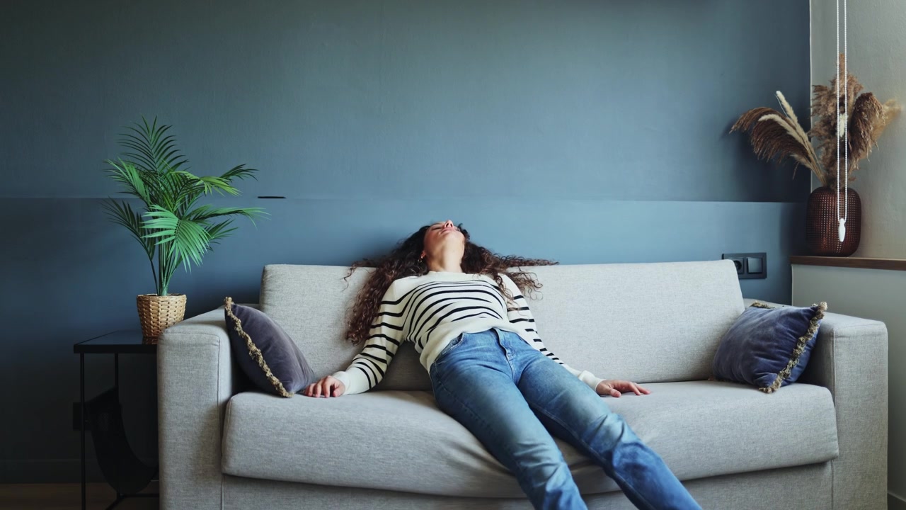 Young Woman Collapsing onto Sofa to Relax at Home