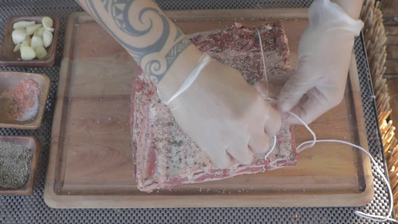 Close up top view of chef tied piece of steak with twine on wooden board of restaurant kitchen.