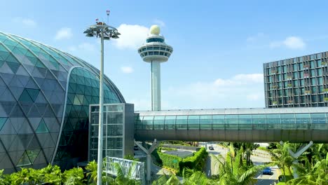 a smooth daytime camera pan reveals a glass-domed airport terminal, lush greenery, and a prominent air traffic control tower under clear blue skies