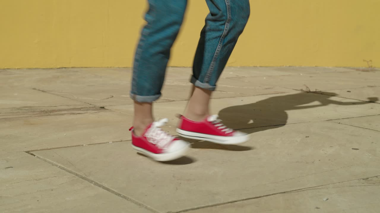 piernas de mujer joven feliz bailando en cámara lenta usando zapatillas converse rojas en un piso de concreto con un fondo amarillo