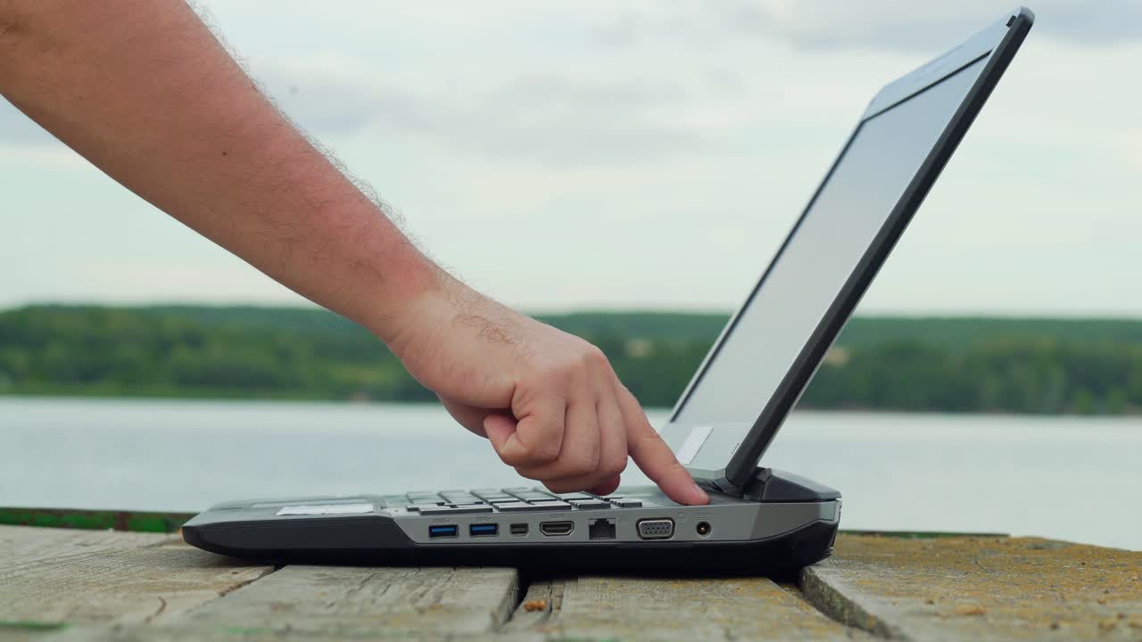 Man's hands using laptop computer. Young man sitting on a wharf and using a notebook