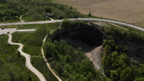 Beautiful-aerial-flight-towards-Devil's-Punch-Bowl-Waterfall-surrounded-by-green-trees-during-sunny-day,Canada