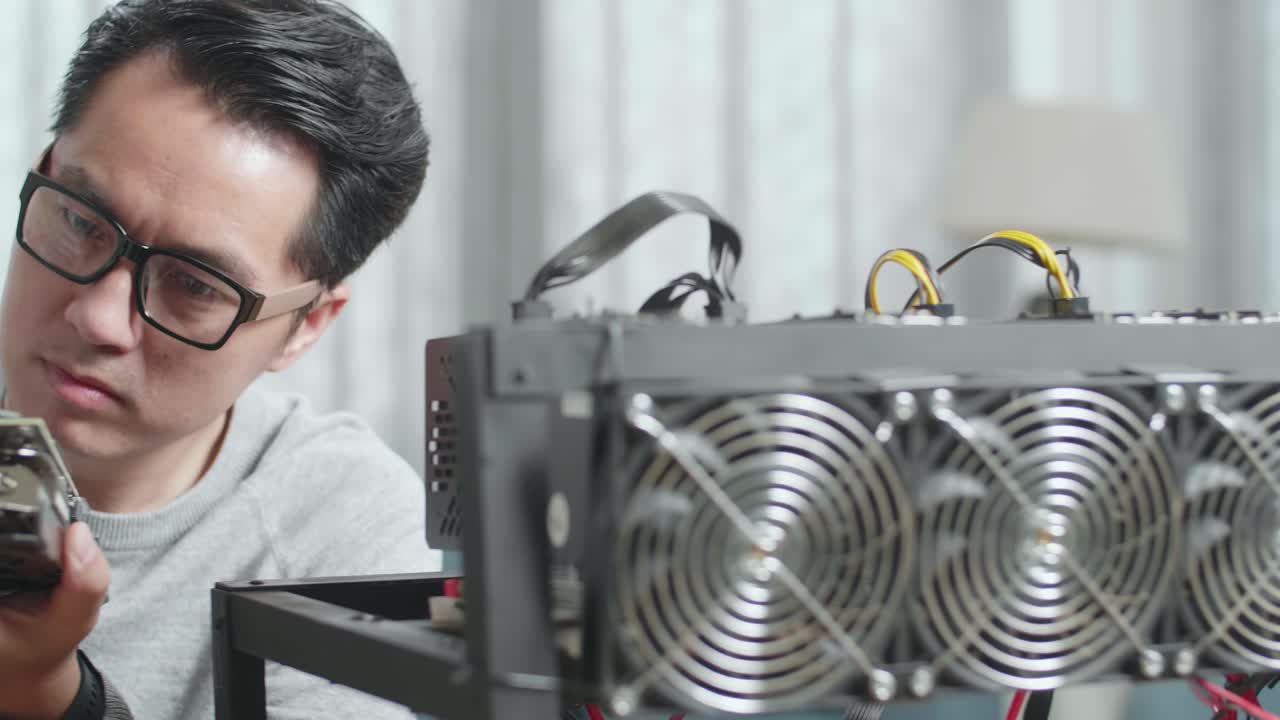 안경을 쓴 아시아 남자가 암호화폐를 채굴하기 위해 그래픽 카드를 청소합니다.