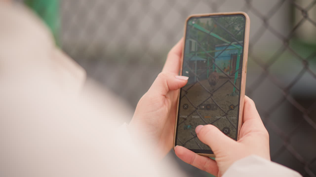 mani che tengono uno smartphone che mostra una mappa, primo piano dell'interfaccia di navigazione cittadina con vista sopra la spalla vicino a una recinzione a catena, un pendolare che tocca lo schermo per controllare il percorso, toni tenui e bokeh delicato, pratico e mirato