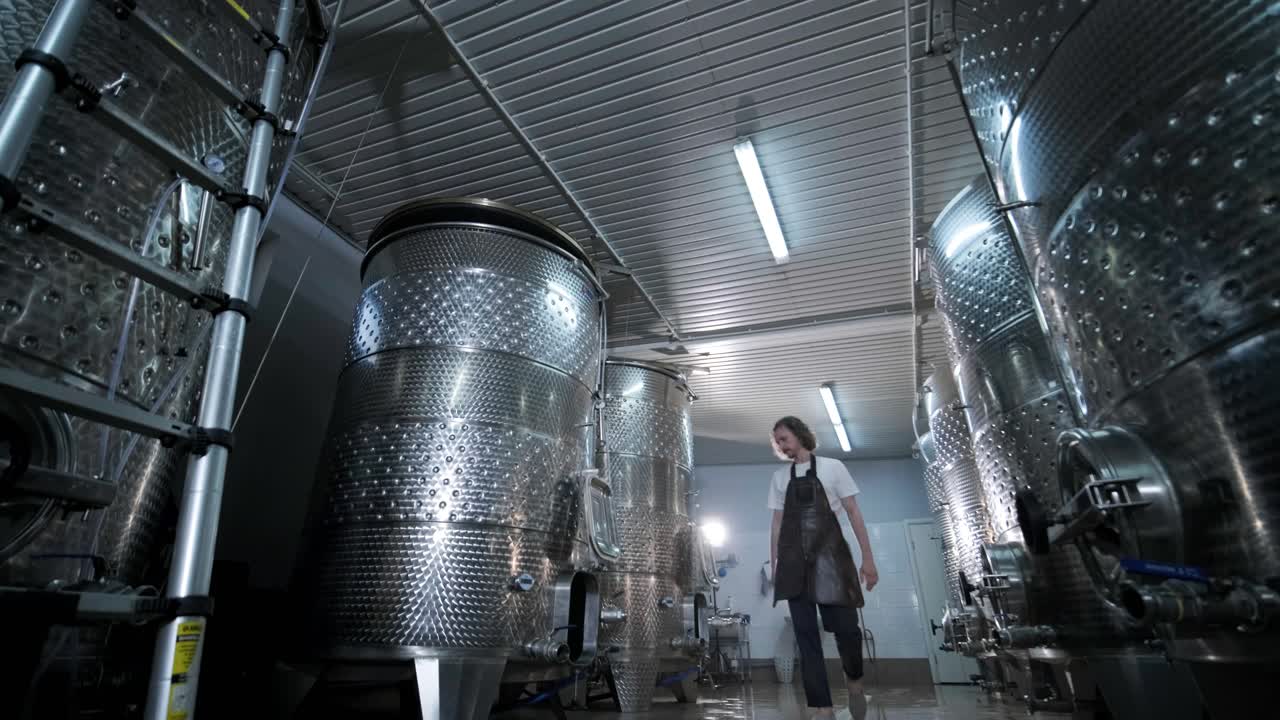 un agricultor o viticultor feliz está caminando en medio de tanques de vino y comprobando un grado de fermentación de la producción de vino de alta calidad en una instalación moderna de elaboración de vino o bodega.