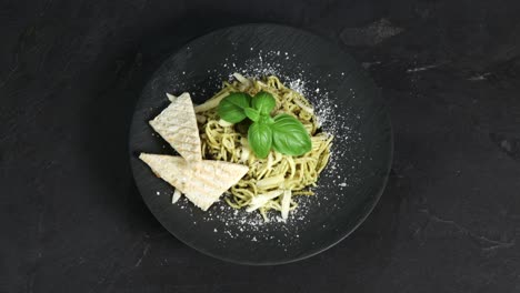 spaghetti with green pesto and cheese garnished with bread and basil are presented on a rotating plate