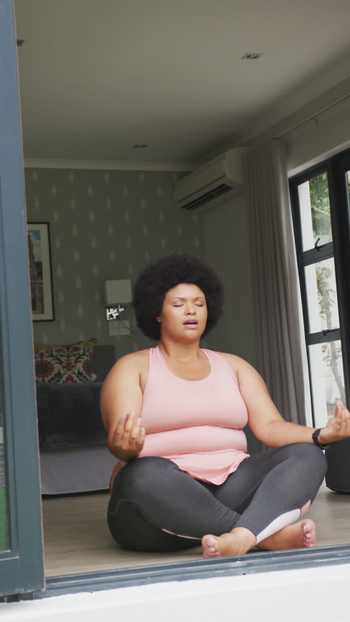 Video verticale di donna birazziale taglia forte che pratica yoga a casa