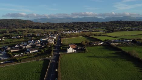 aerial view circling over small town welsh community farmland with snowdonia mountain range on the horizon