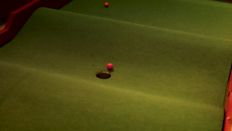 una pelota de golf roja rueda en un campo de golf en miniatura, iluminada por una iluminación cálida, moviéndose hacia el agujero en una superficie verde