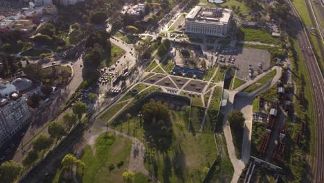 Toma-Aérea-De-Arriba-Hacia-Abajo-Del-área-Del-Parque-Rural,-Conducción-De-Automóviles-Y-Edificio-Del-Centro-De-Exposiciones-De-Buenos-Aires-Al-Atardecer