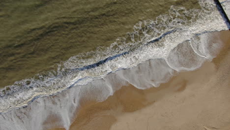 Aerial-cinematic-spin-right-looking-down-peaceful-golden-colored-beach-from-with-waves-crashing-Bournemouth-UK-English-Channel-surf-Pacific-Ocean