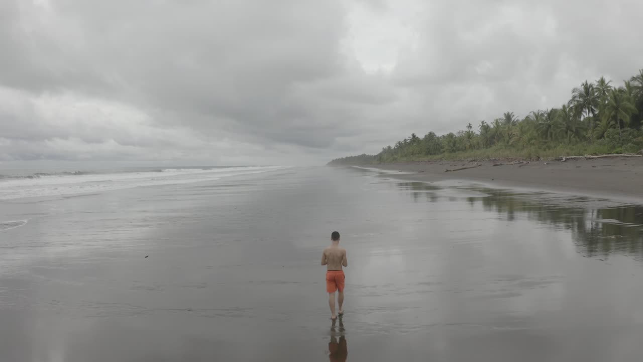 vuelo aéreo sobre un joven caminando en una playa vacía en colombia