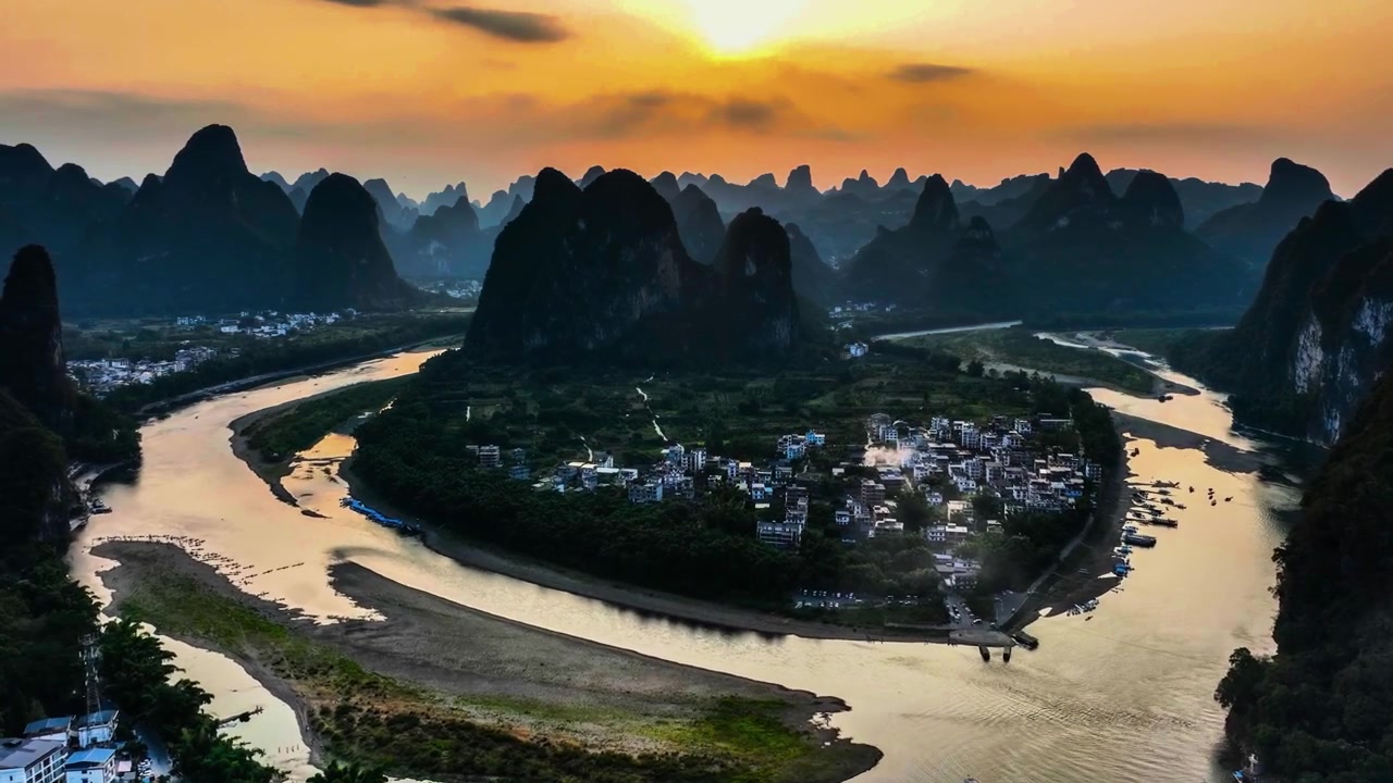 A luz dourada do pôr do sol ilumina a água do rio, picos íngremes e um povoado rural