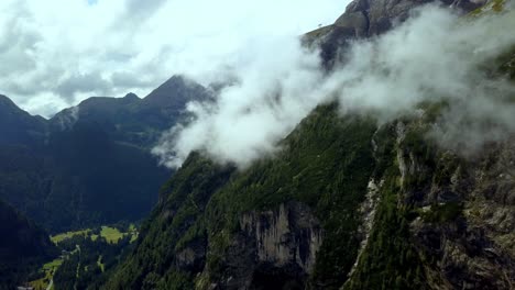 Cloudy-Dolomite-mountains-with-green-foliage-in-northern-Italy-with-meadow-below-on-a-winter-day,-Aerial-drone-advance-shot