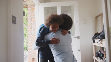 smartly dressed middle aged black man man kneeling down in hallway by the front door to hug and say goodbye to his son before he leaves for school in the morning, low angle