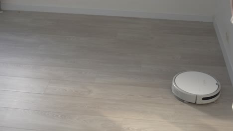 white robotic vacuum cleaner on laminate floor cleaning dust in living room interior. smart housekeeping technology.