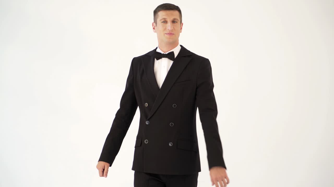 handsome man in a suit with bow-tie is posing in front of a mirror at the exit of the room. Parody of the gentleman on the white background