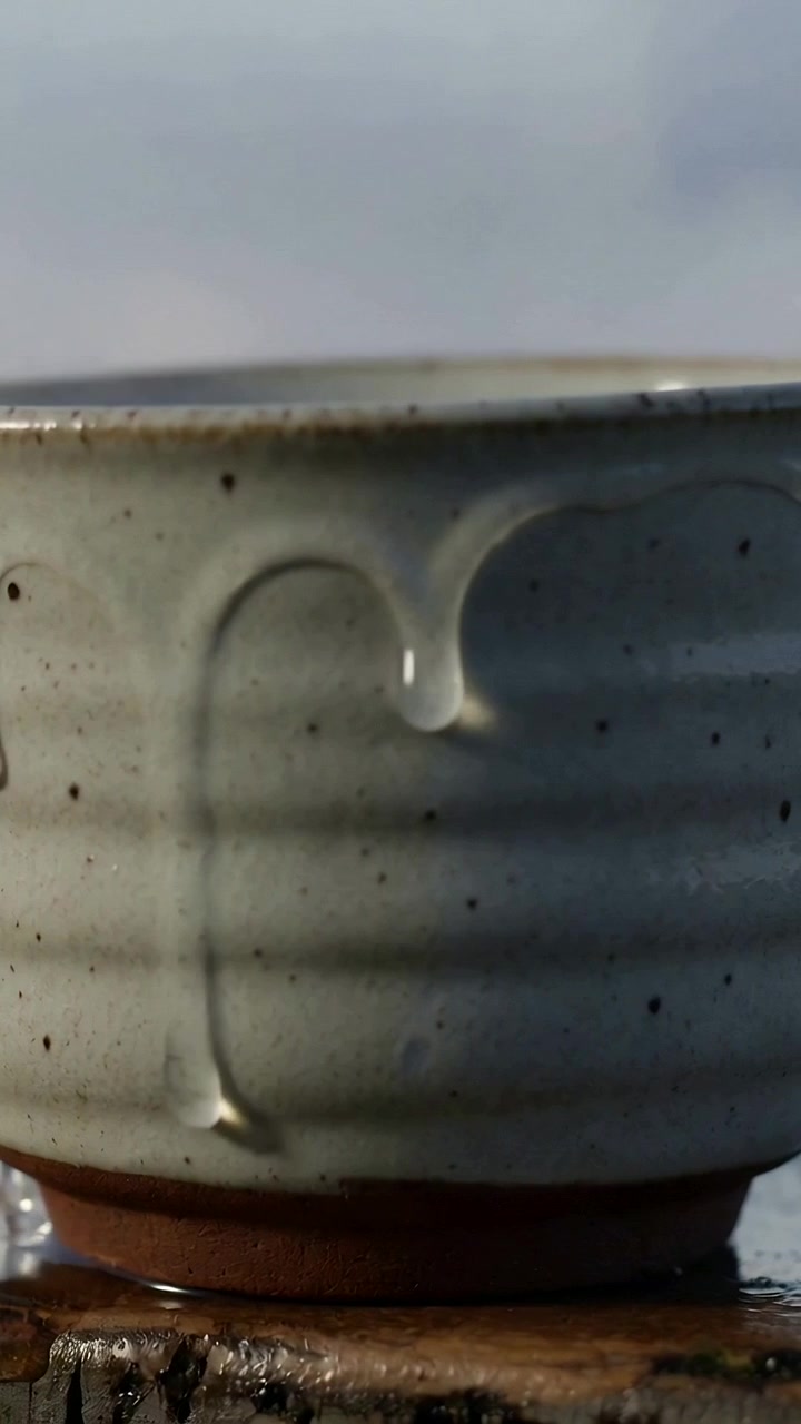 Vertical video: Filming glazed cup shedding thick glaze while gravity pulling bead onto wood slab