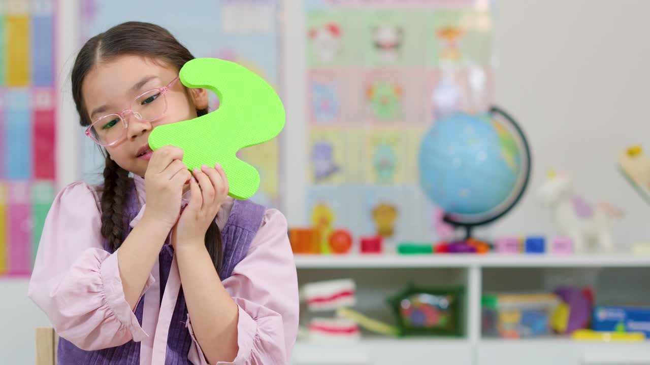 Smiling girl with glasses presents foam number two in colorful, well-lit classroom, static camera