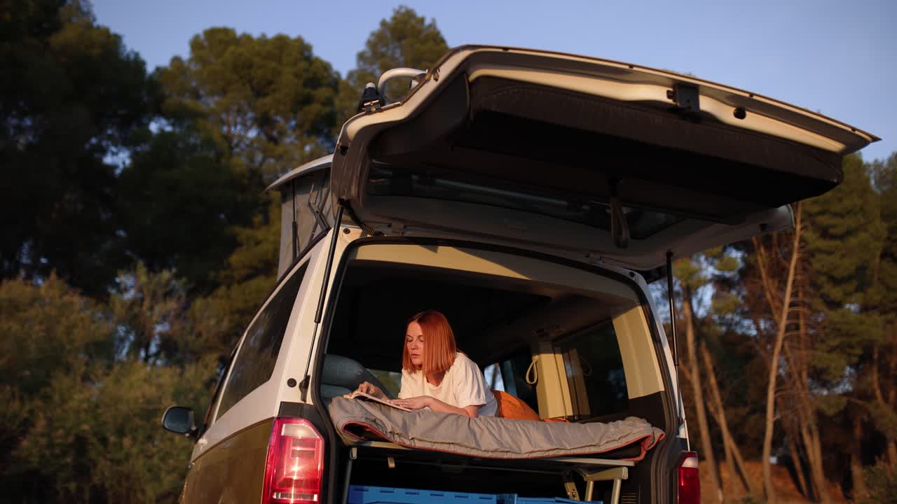 Giovane donna che legge un libro nel retro di un camper