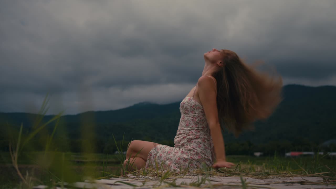 Woman Sitting in a Field, Mountains in Background
