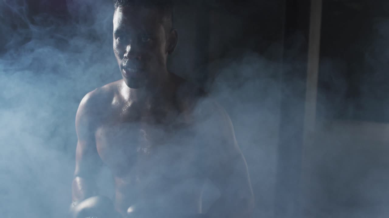 어두운 연기가 가득한 방에서 권투 장갑을 입은 아프리카계 미국인 남자가 주먹을 치고 있습니다.