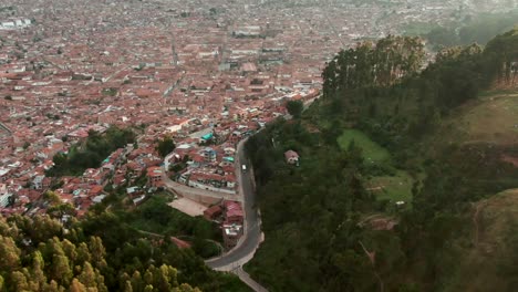 Dolly-in-aerial-over-eucalyptus-tree-forest-reveals-the-stunning-city-of-Cusco,-Peru