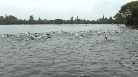 Los-Competidores-De-Inicio-De-Natación-De-Triatlón-Se-Dirigen-A-La-Primera-Boya-En-Un-Día-Gris-Con-Lluvia-Ligera---Lago-Rua,-Christchurch