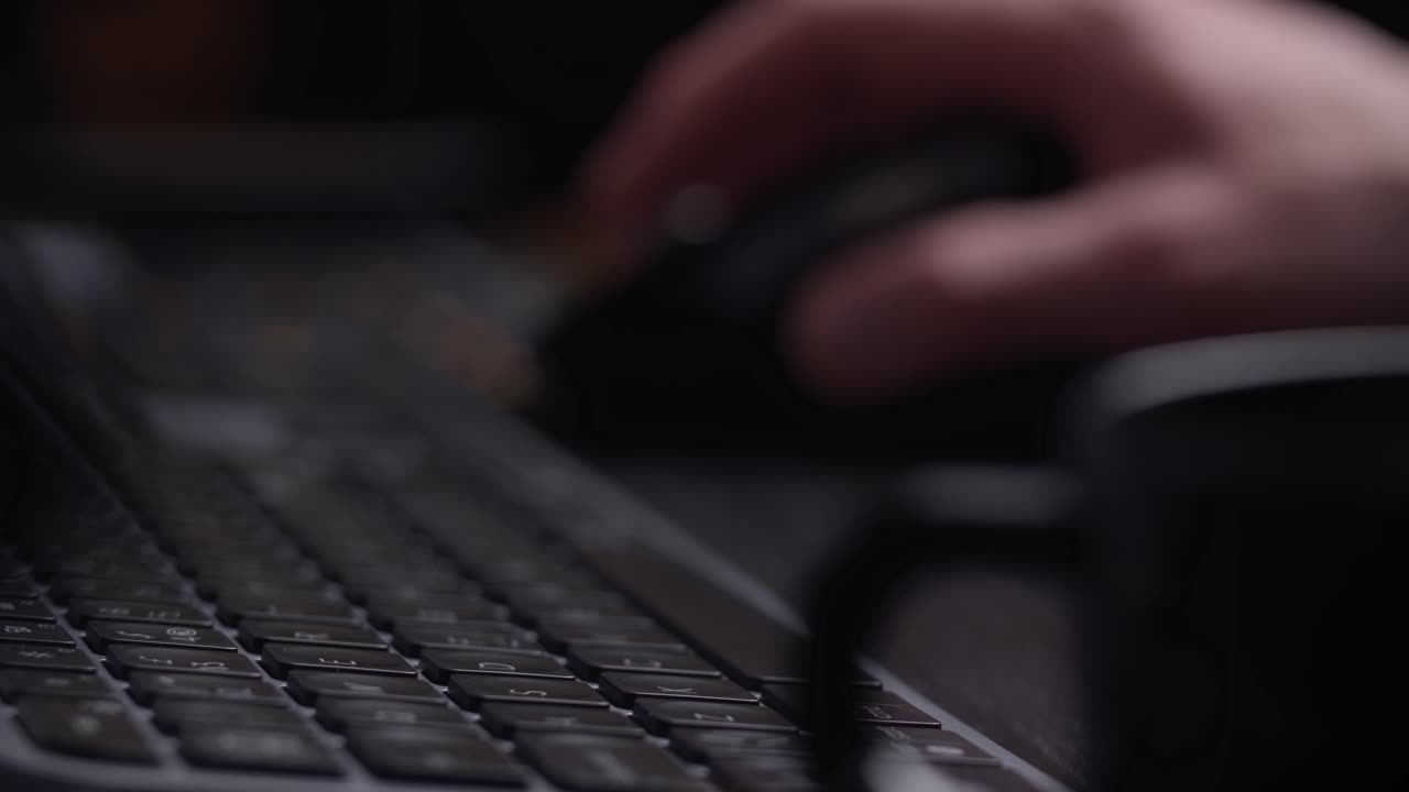 Hand working with mouse, keyboard from a side perspective with blurred background.