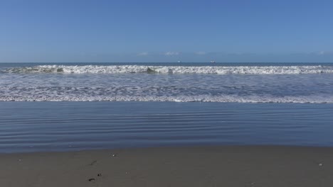 Small-waves-from-incoming-tide-roll-over-patterns-in-sand---New-Brighton-Beach,-New-Zealand