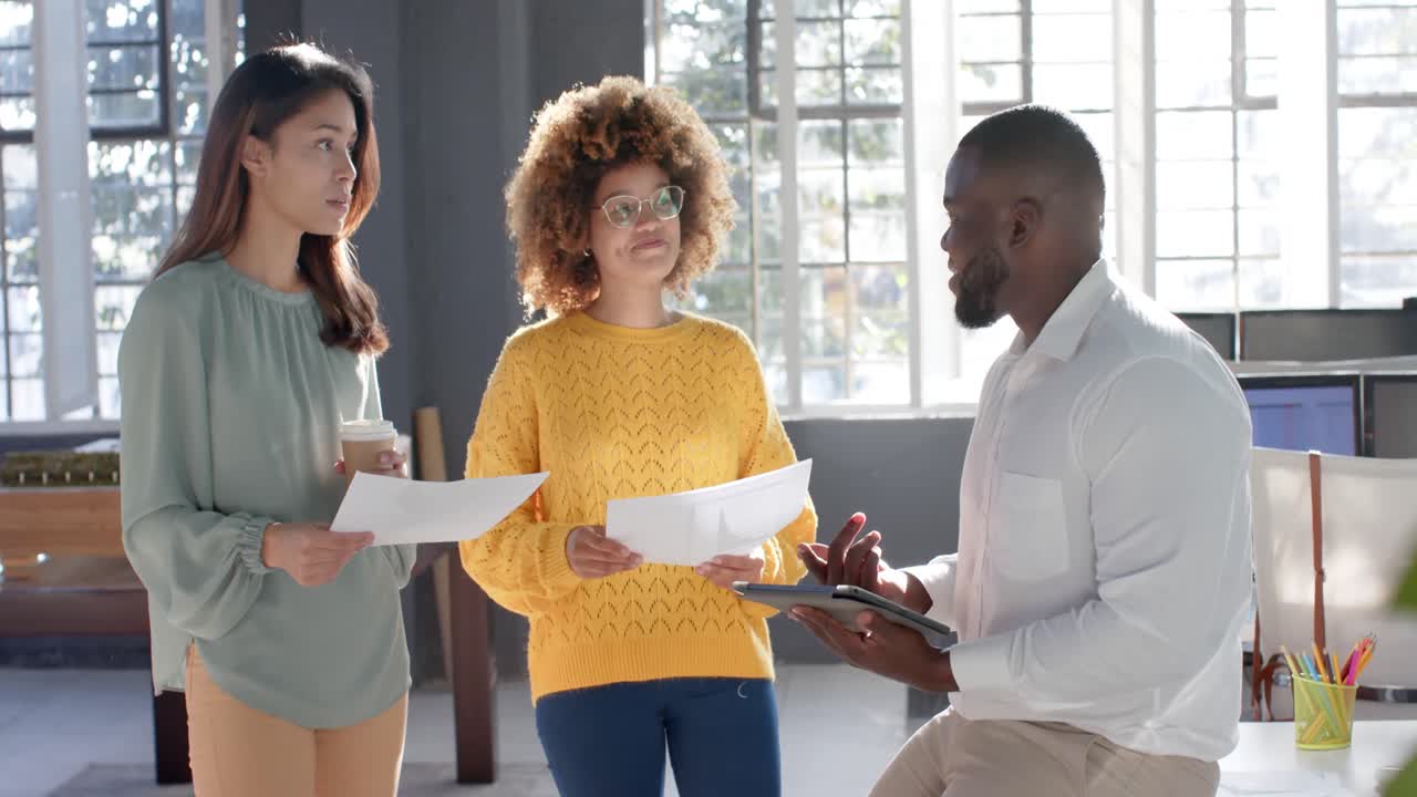 Busy diverse colleagues with documents and tablet discussing work in sunny office, slow motion