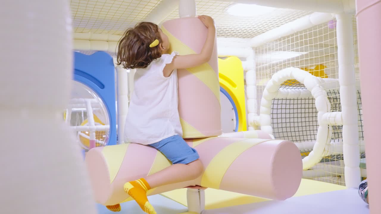 A little child spinning on marshmallows on a colorful indoor playground with her mom