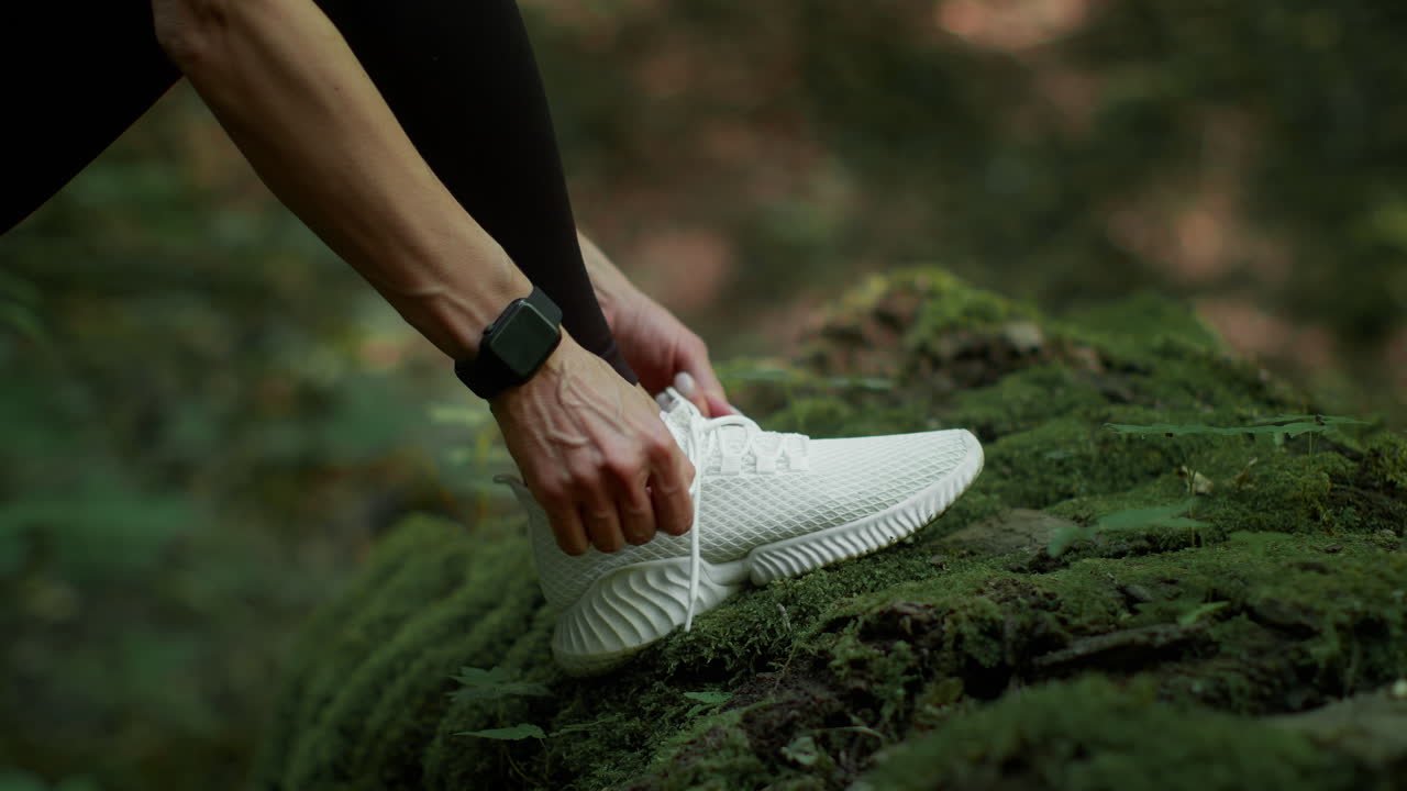 Persona che allaccia i lacci di una sneaker bianca in una foresta muschiosa