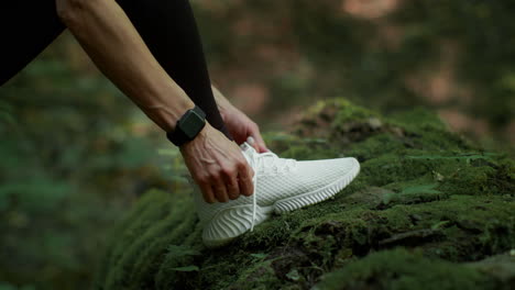 person tying shoelaces on a white sneaker in a mossy forest