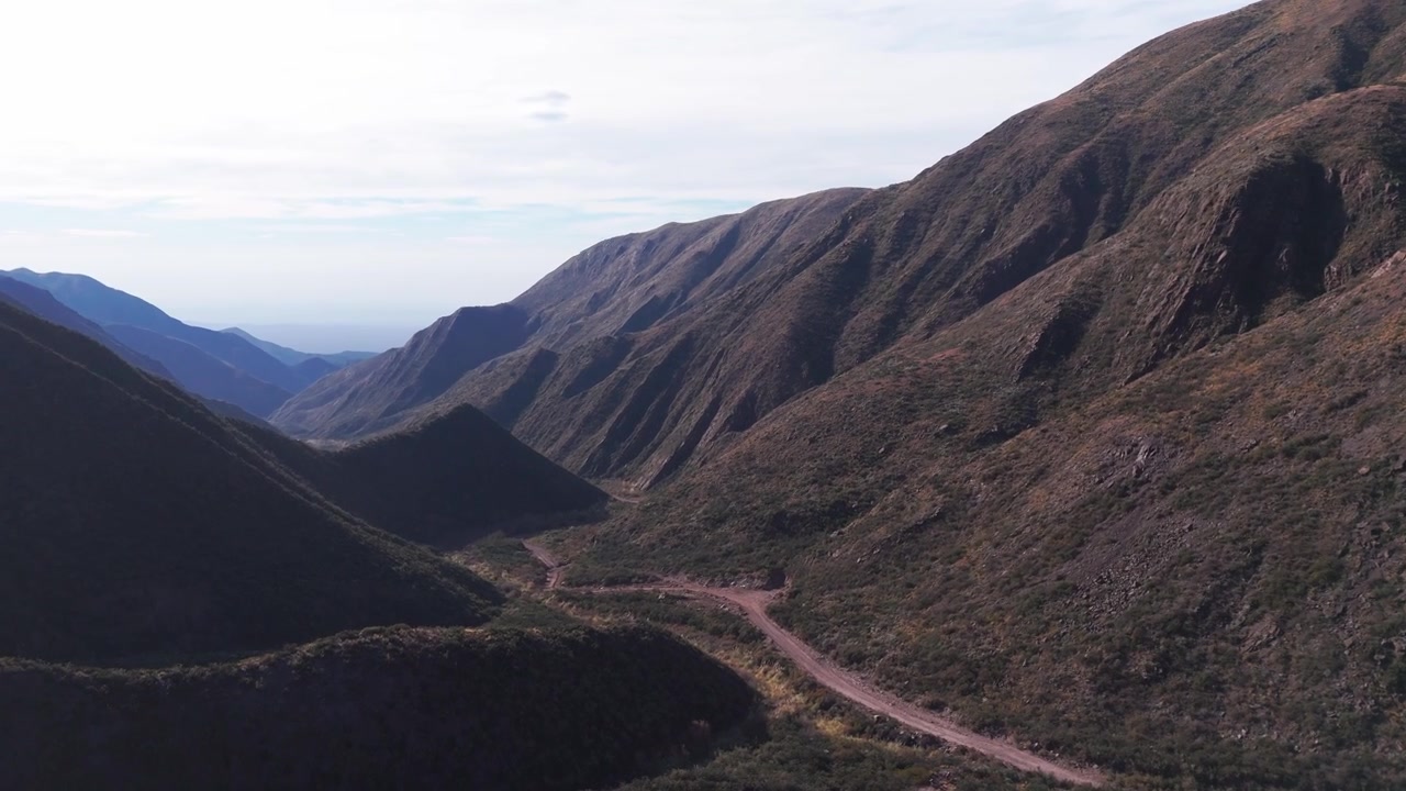 Ripresa aerea con drone che rivela la cima di una collina in mezzo a montagne erbose in Argentina.