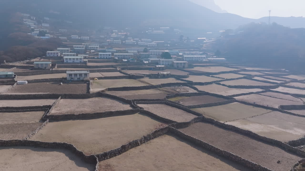 Drone shot of Phortse Village at sunrise with dry farming lands, morning dew, smoke haze, diverse architecture buildings, and religious setting in Himalayas peace and calm nature