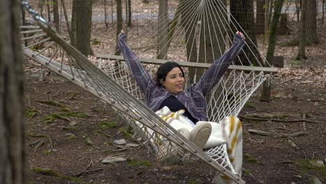 peaceful young female swinging in woodland hammock having relaxed lazy time alone