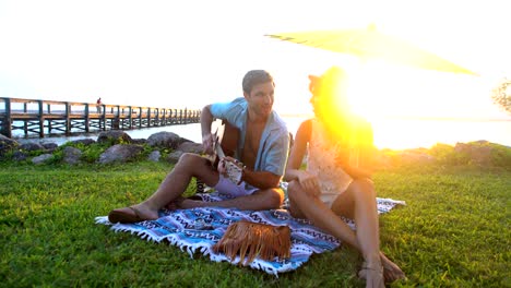 multi ethnic couple playing guitar at beach picnic